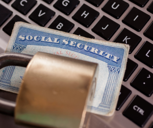 A padlock securing a Social Security card placed on a laptop keyboard.